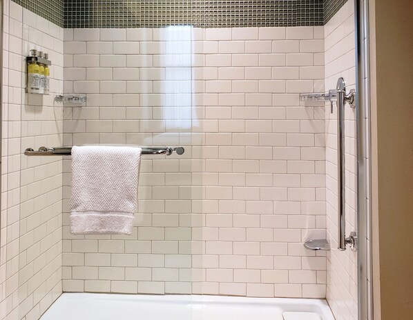 Un espacio de ducha pequeño y cerrado con azulejos blancos, una puerta de cristal y un perchero con una toalla blanca.