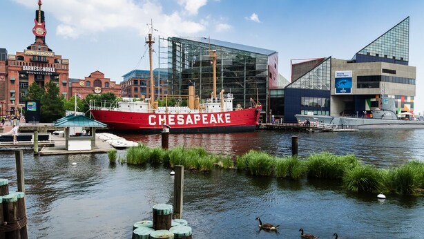 A red ship named 'CHESAPEAKE' docked at a marina with modern buildings in the background.