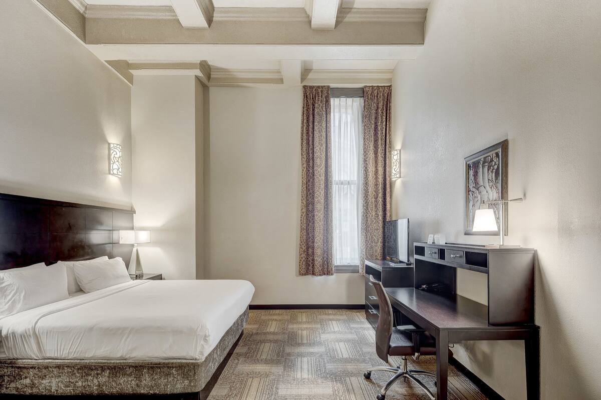 A hotel room with a bed, desk, chair, and a window with curtains.