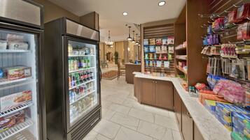 A hotel lobby with a self-service beverage fridge, a reception desk, and a variety of snacks and toiletries on shelves.