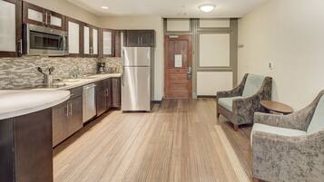 Una cocina moderna con electrodomésticos de acero inoxidable, piso de madera y una zona de estar con dos sillones y una mesita.
