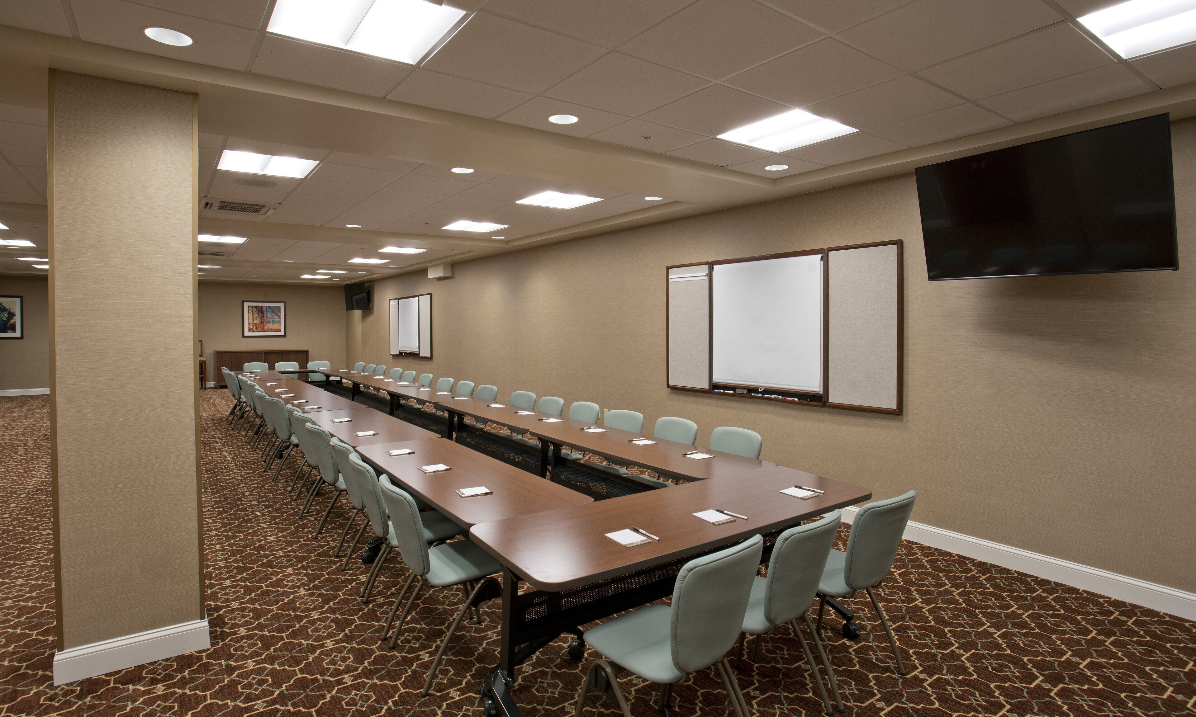 Un salón de conferencias con una larga mesa, sillas, una pantalla de proyector y una pizarra.