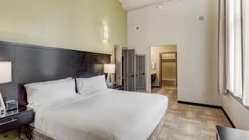 Quarto de hotel com uma cama grande, mesas de cabeceira, escrivaninha e um guarda-roupa.
