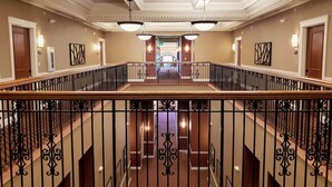 A hotel lobby with a central staircase, a reception desk, and a view of the parking area.
