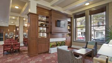 Un vestíbulo de hotel con un mueble de entretenimiento grande de madera, un acuario y una zona de estar con vista a la calle.