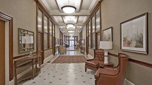 A hotel hallway with a patterned floor, leather chairs, a round table, and framed artwork on the walls.