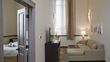 A hotel room with a bed, a desk with a computer, a sofa, a lamp, and a window with curtains.