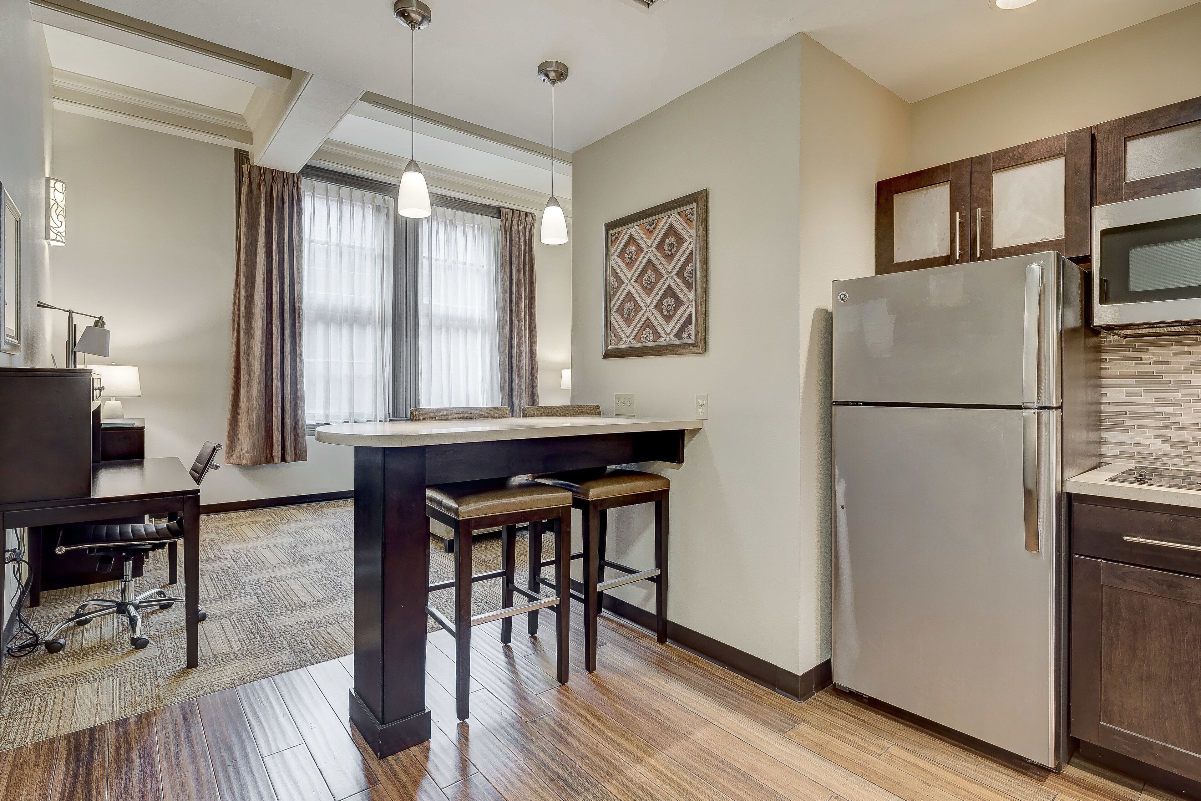 Una cocina moderna con una isla central, taburetes de bar, un refrigerador y un microondas.