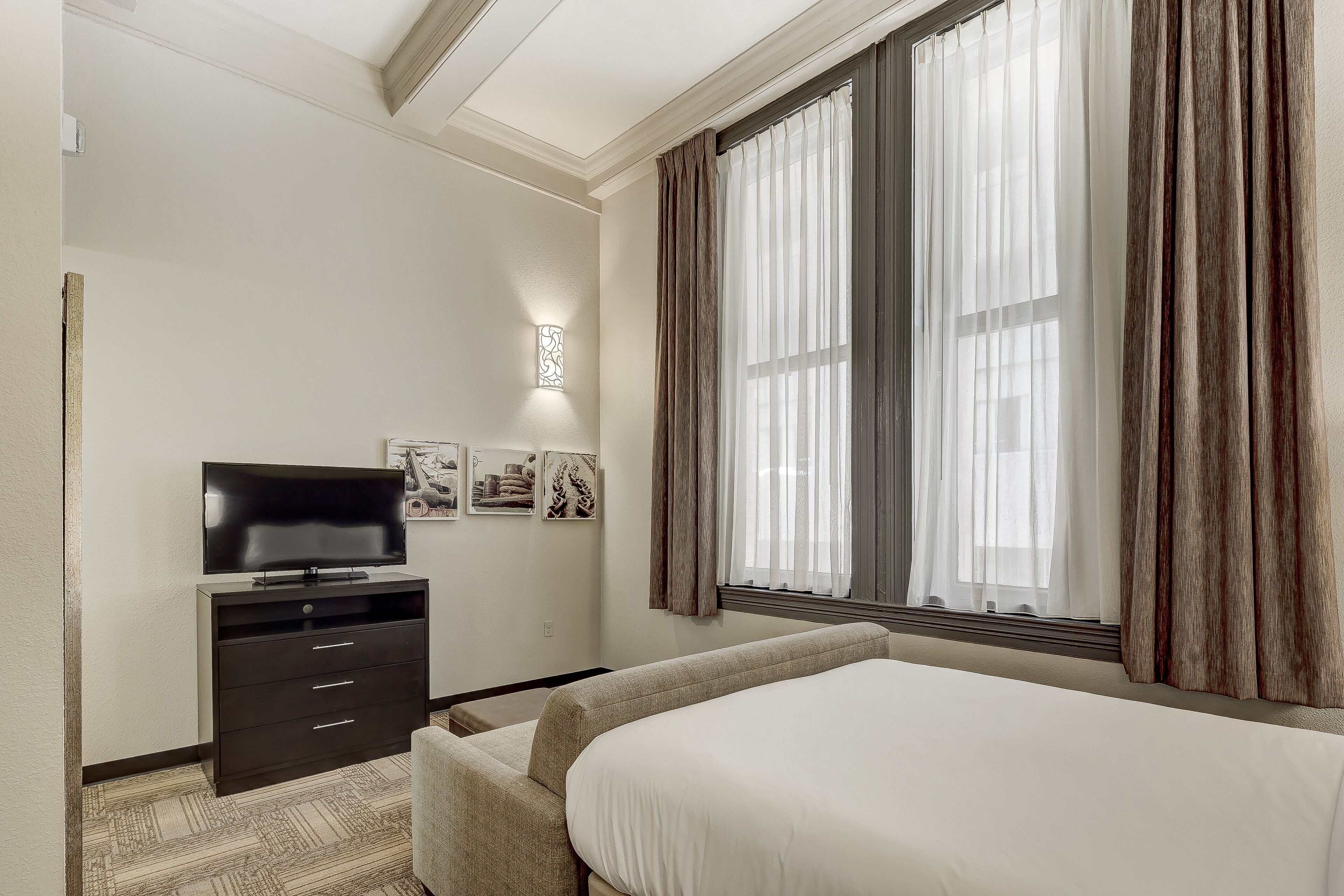Ein Hotelzimmer mit einem Bett, einem Fernseher auf einem Schrank, einer Kommode und einem Fenster mit Vorhängen.