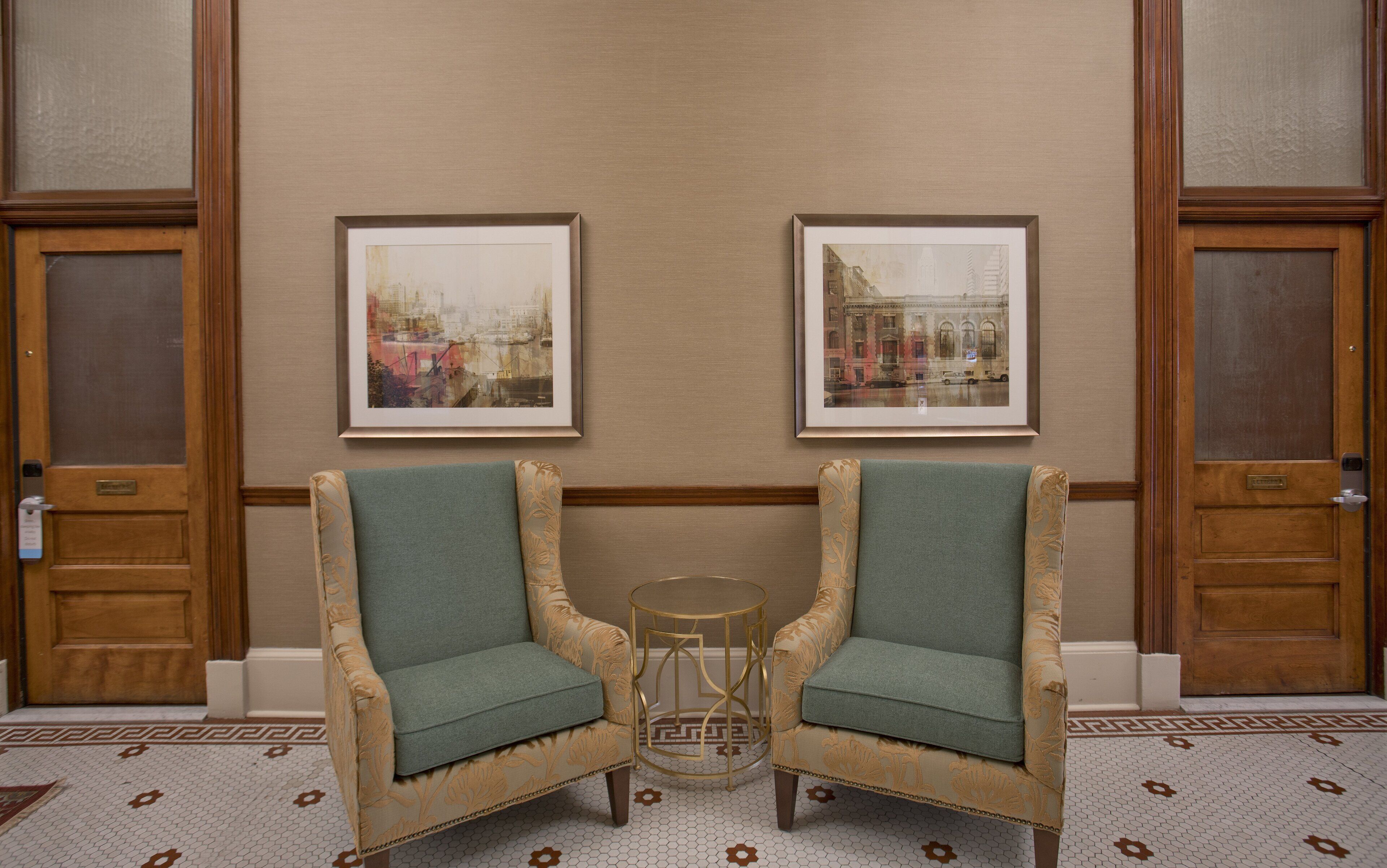 A room with two armchairs, a small round table, and two framed pictures on the wall.