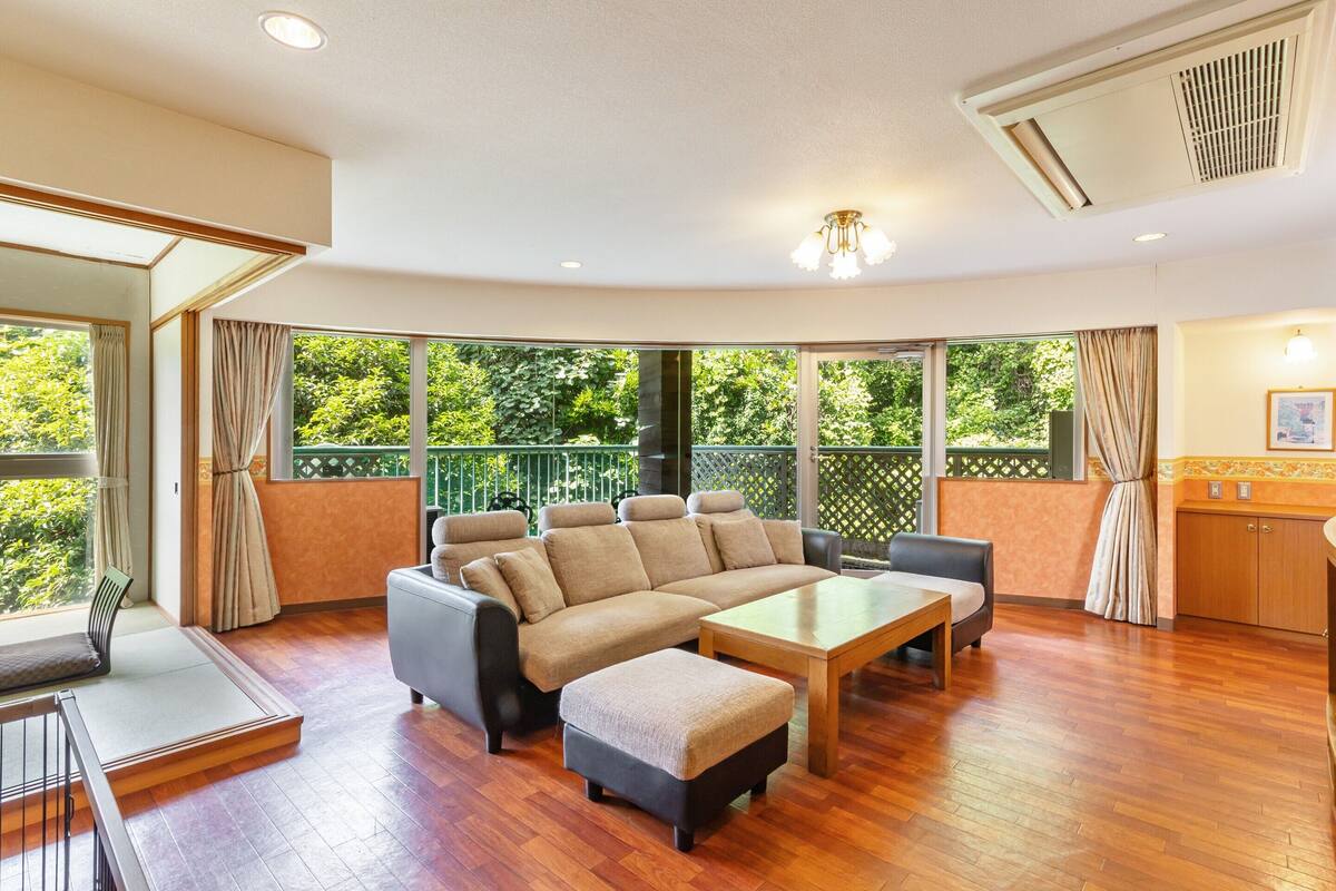 Amplia sala de estar con un sofá seccional grande, una mesa de centro de madera y un balcón con vistas a la vegetación.