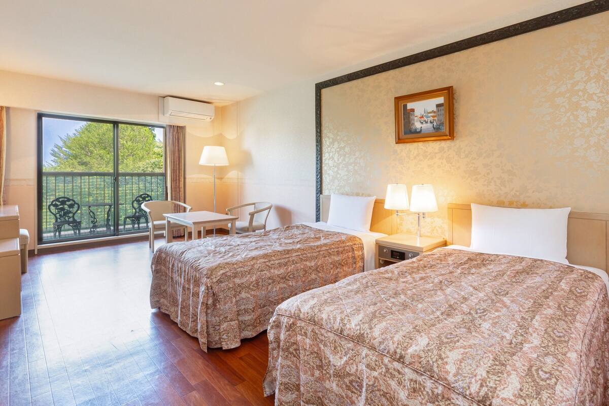 Habitación de hotel con dos camas, un balcón con mesa y sillas, y un cuadro en la pared.