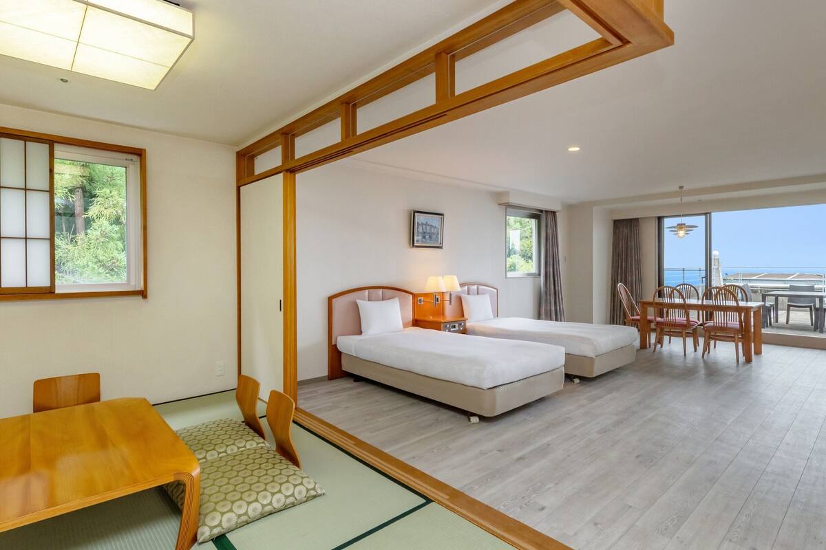 Habitación de hotel con dos camas, una mesa de comedor y vista al mar.