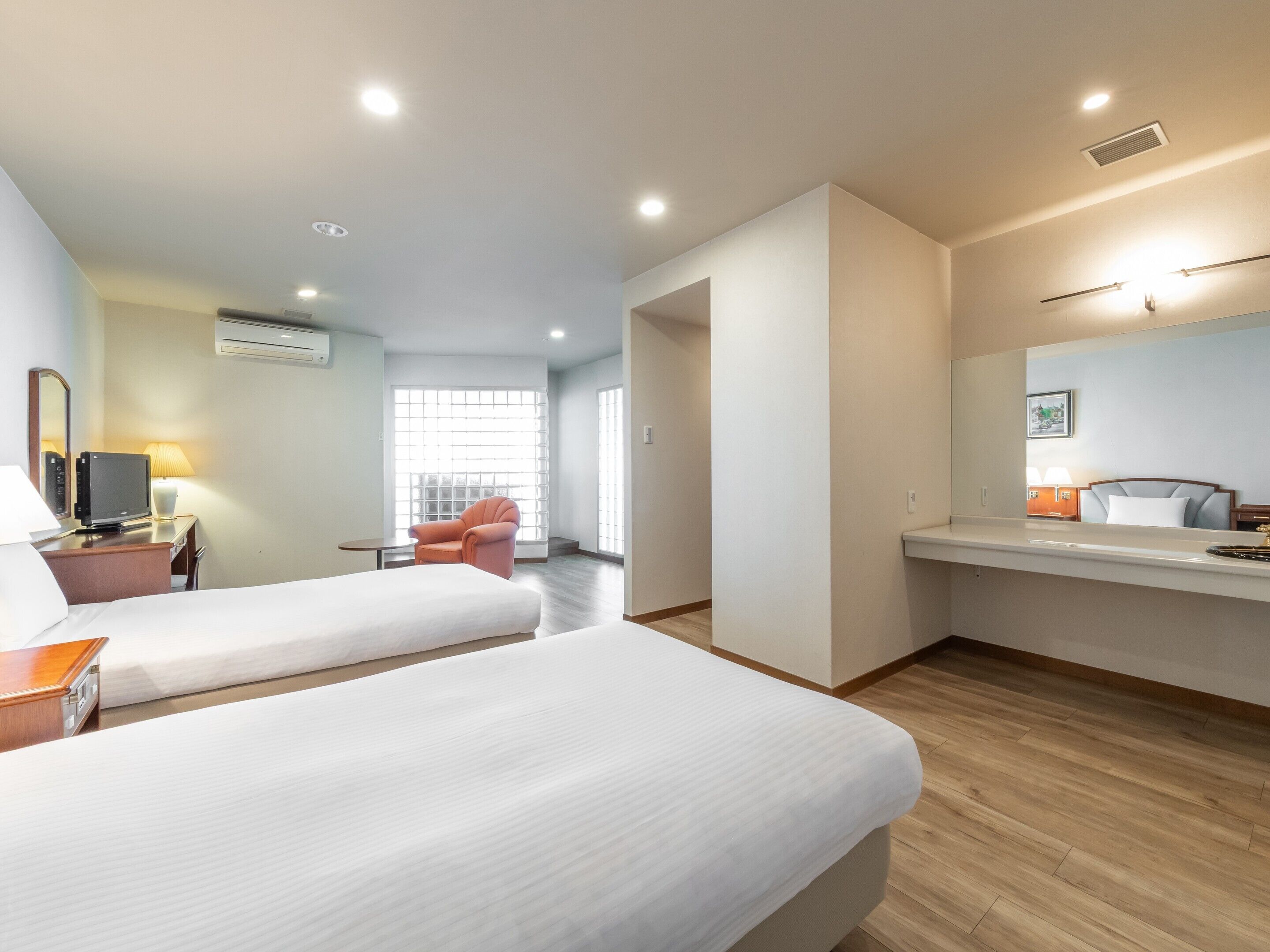 A hotel room with two beds, a desk with a computer, a chair, and a large window.