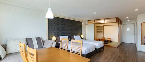 A modern hotel room with a wooden dining table, two beds, a sofa, and a separate dining area.