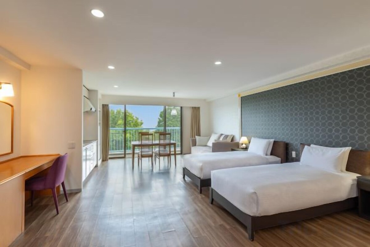 A hotel room with two beds, a desk, and a balcony.