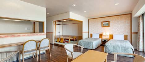 A hotel room with a bed, two bedside tables, a desk, a chair, a sofa, and a small balcony.