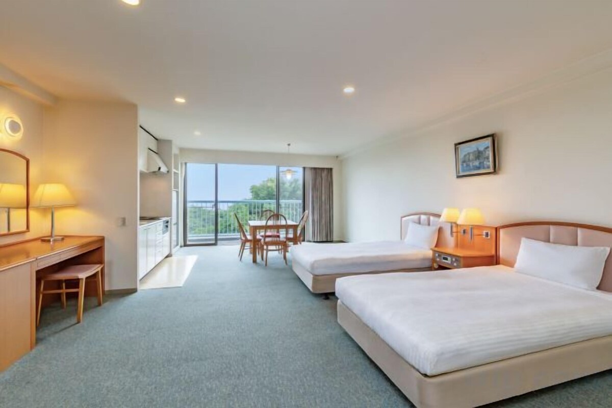 Une chambre d’hôtel avec deux lits, un bureau, une chaise et un balcon avec vue.