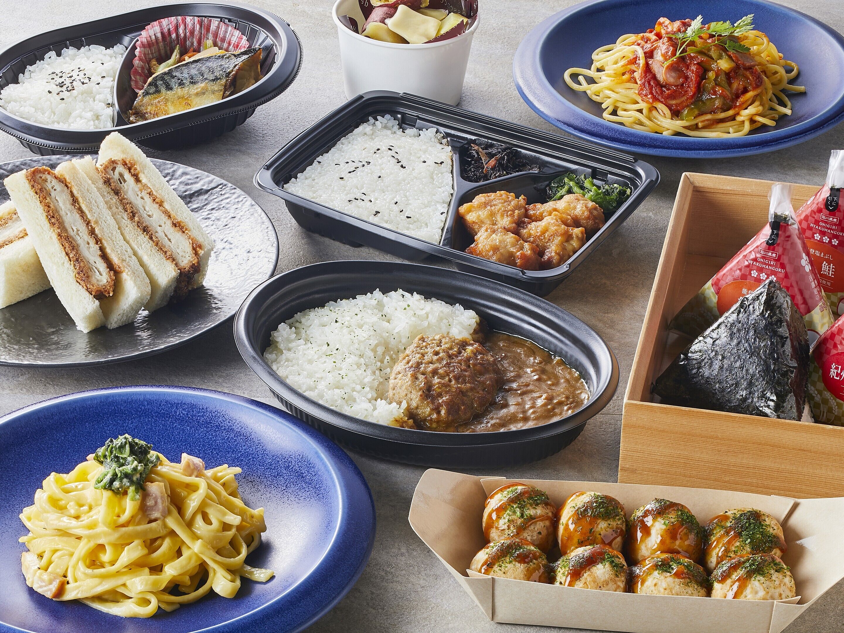 Verschiedene japanische Gerichte wie Reis, Nudeln und Fisch sind auf einem Tisch angerichtet.