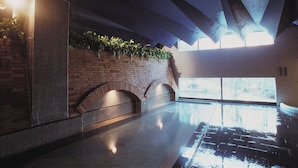 Een modern binnenzwembad met een bakstenen muur, gebogen zitplaatsen en een groot raam voor natuurlijk licht.