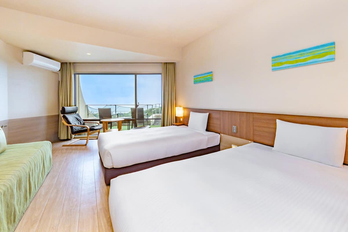 Een hotelkamer met twee bedden, een zithoek met een stoel en tafel, en een groot raam met uitzicht.