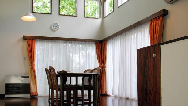 A dining area with a table and chairs, large windows with curtains, and an air conditioning unit. - Wan Wan Paradise Izukogen (Ito)