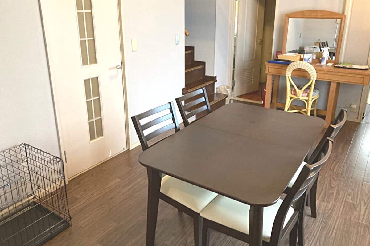 Een eetkamer met een donker houten tafel en stoelen, een klein keukenhoekje met een houten aanrecht en een spiegel, en een deur naar een andere kamer.