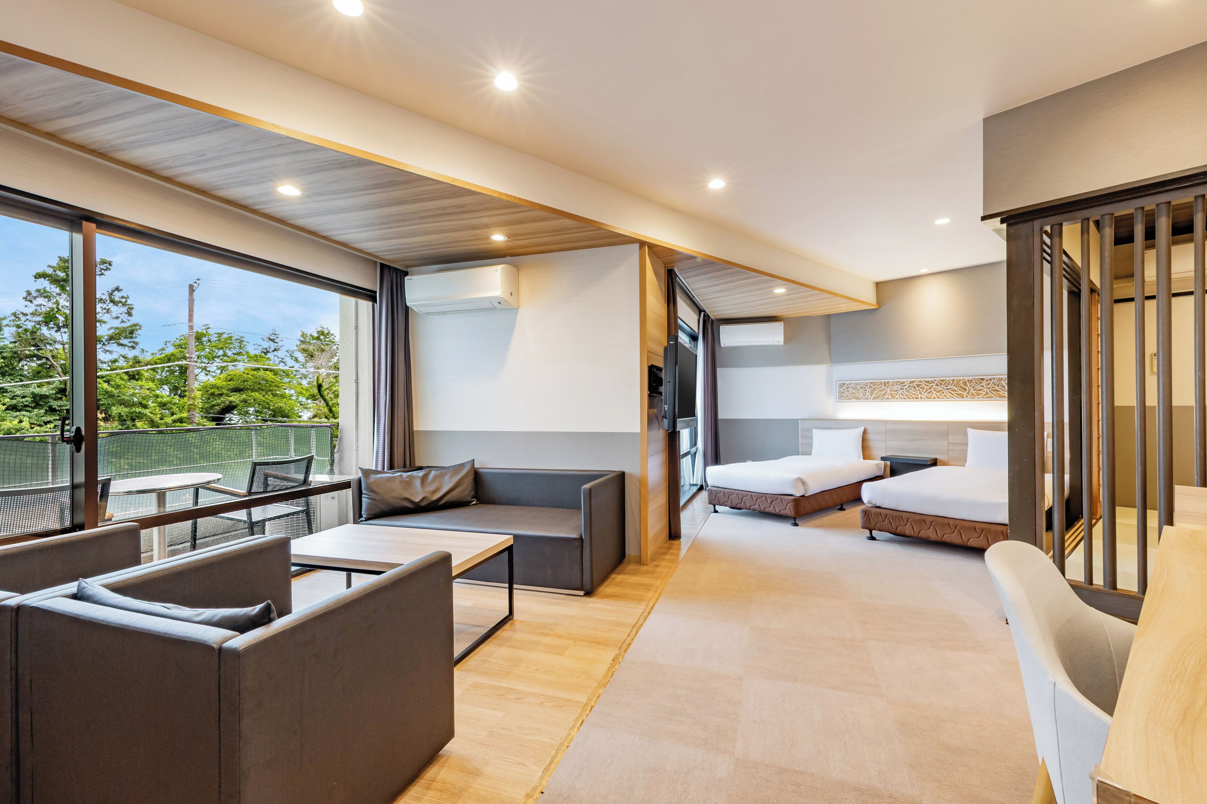 A modern hotel room with a balcony, a sofa, a bed, and a TV.