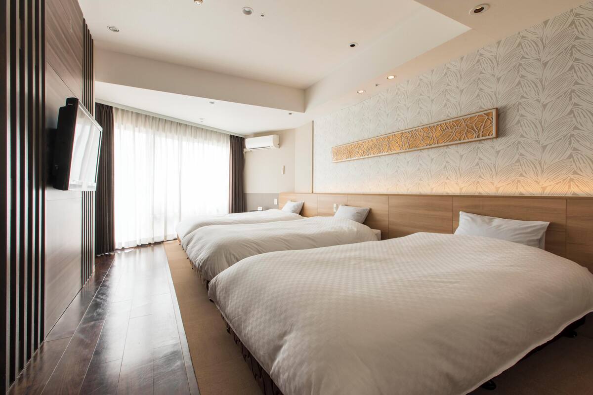 Een hotelkamer met twee bedden, een groot raam met gordijnen, een flatscreen televisie aan de muur en een decoratief paneel.