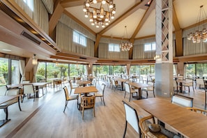 A spacious dining area with multiple tables and chairs, large windows offering views of the outdoors, and a high ceiling with wooden beams and modern lighting fixtures. - Wan Wan Paradise Izukogen (Ito)