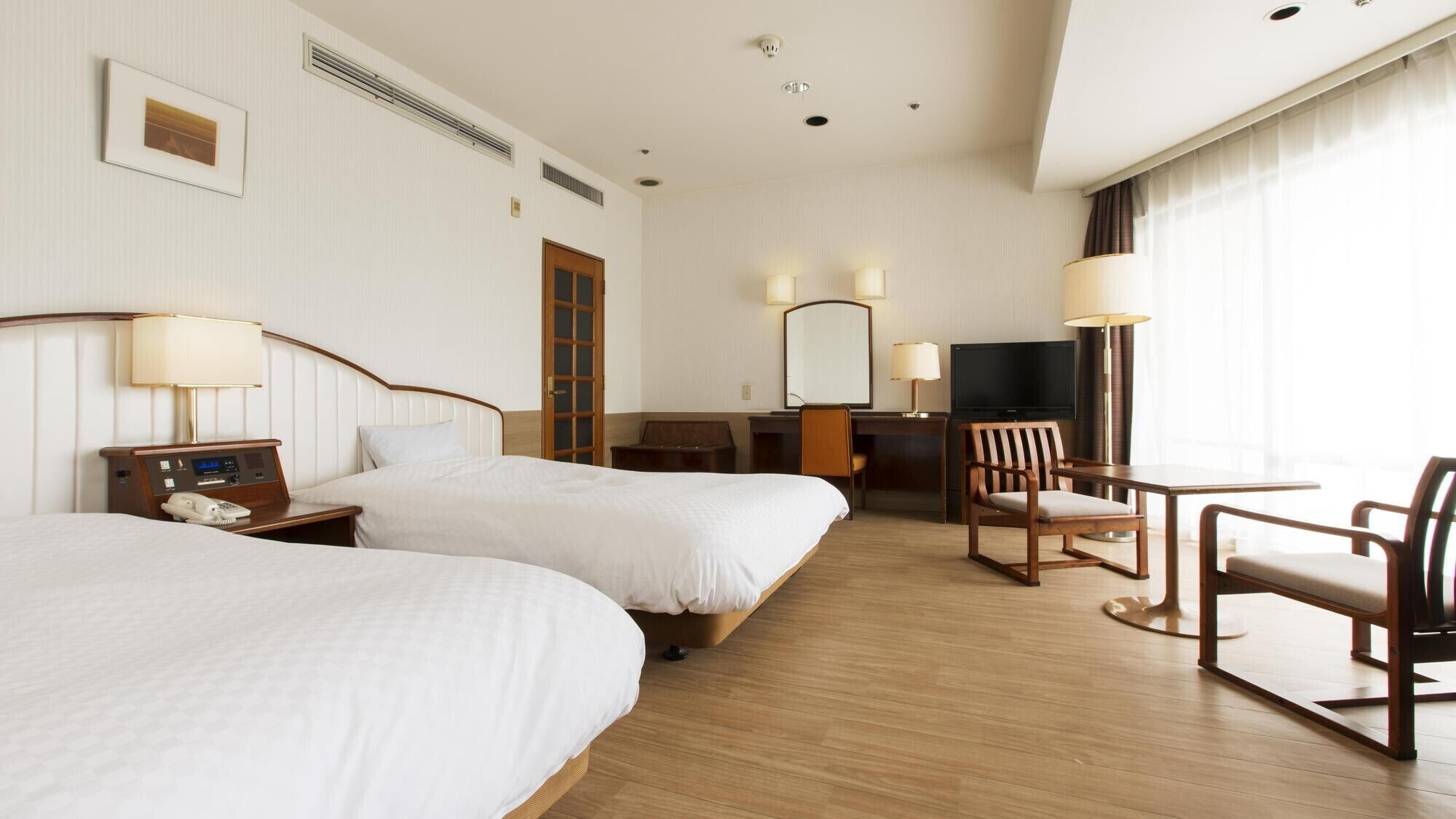Ein Hotelzimmer mit zwei Betten, einem Schreibtisch, einem Stuhl, einem Fernseher und einem Fenster mit Vorhängen.