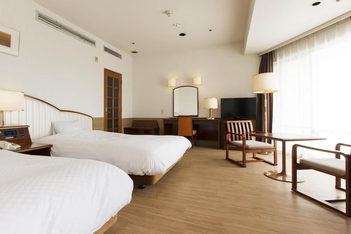 A hotel room with two beds, a desk, a chair, a TV, and a window with curtains.