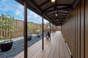 Un espacio al aire libre cubierto con piso de madera, macetas negras y un cerco de madera.