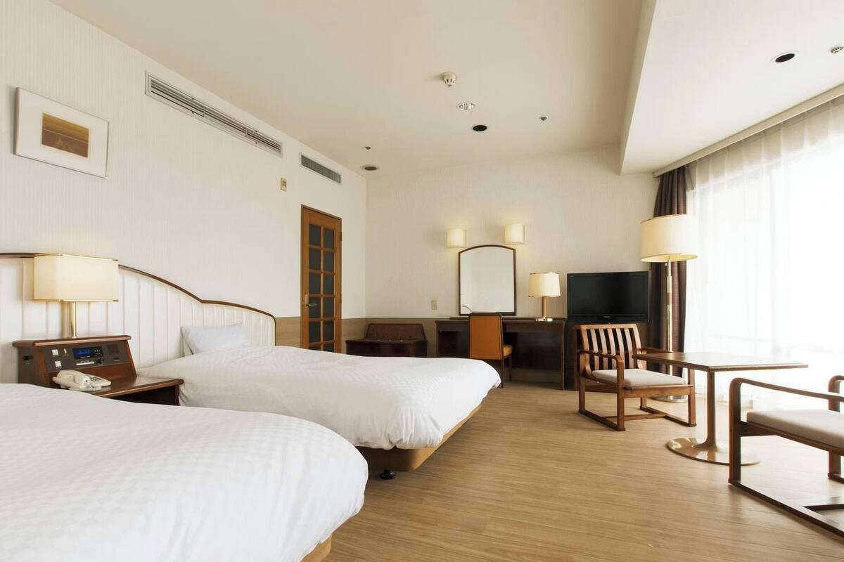 Een hotelkamer met twee bedden, een bureau, een stoel, een televisie en een lamp.