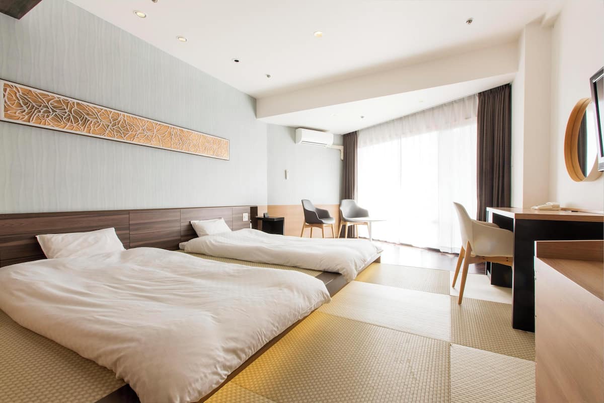 Een hotelkamer met twee bedden, een bureau, een stoel en een groot raam met gordijnen.
