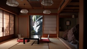 A traditional Japanese room with tatami flooring, a low table, two chairs, and a view of a waterfall through a sliding door. - Meiseki No Yado Kagetsu (Fuefuki)