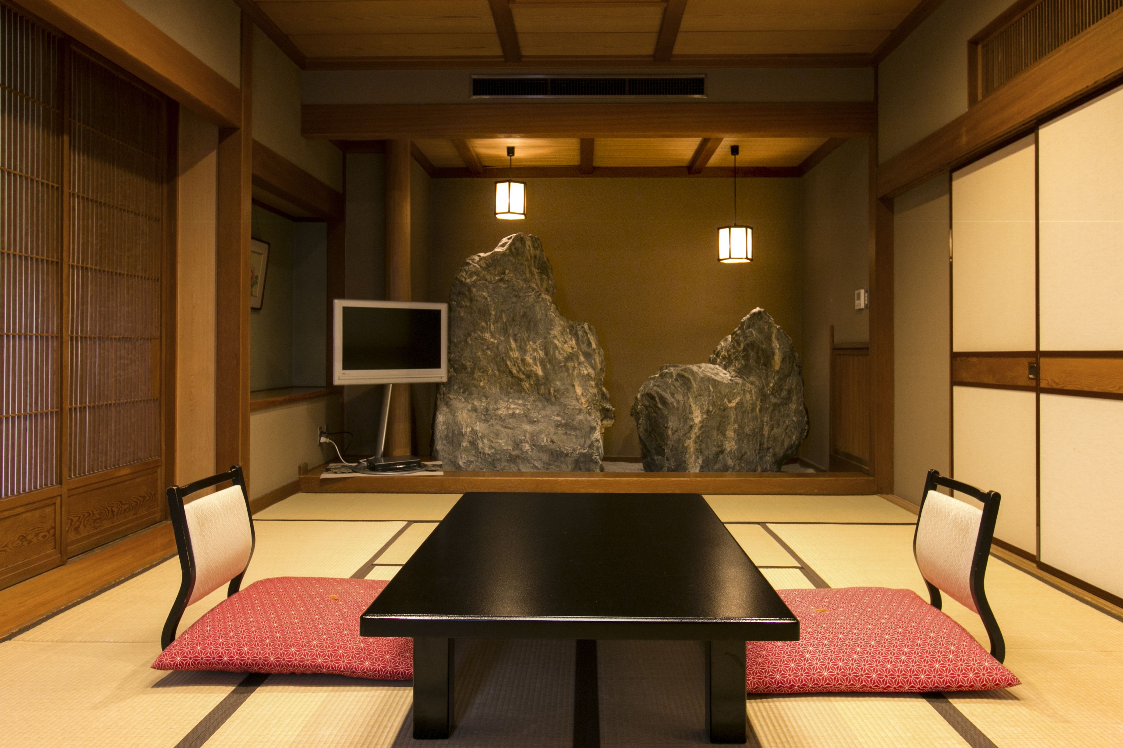 A traditional Japanese room with tatami flooring, a low table, two chairs, and a television.