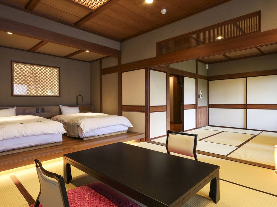 Una habitación de estilo japonés tradicional con suelo de tatami, dos camas con ropa de cama blanca, una mesita baja y un puertas correderas.