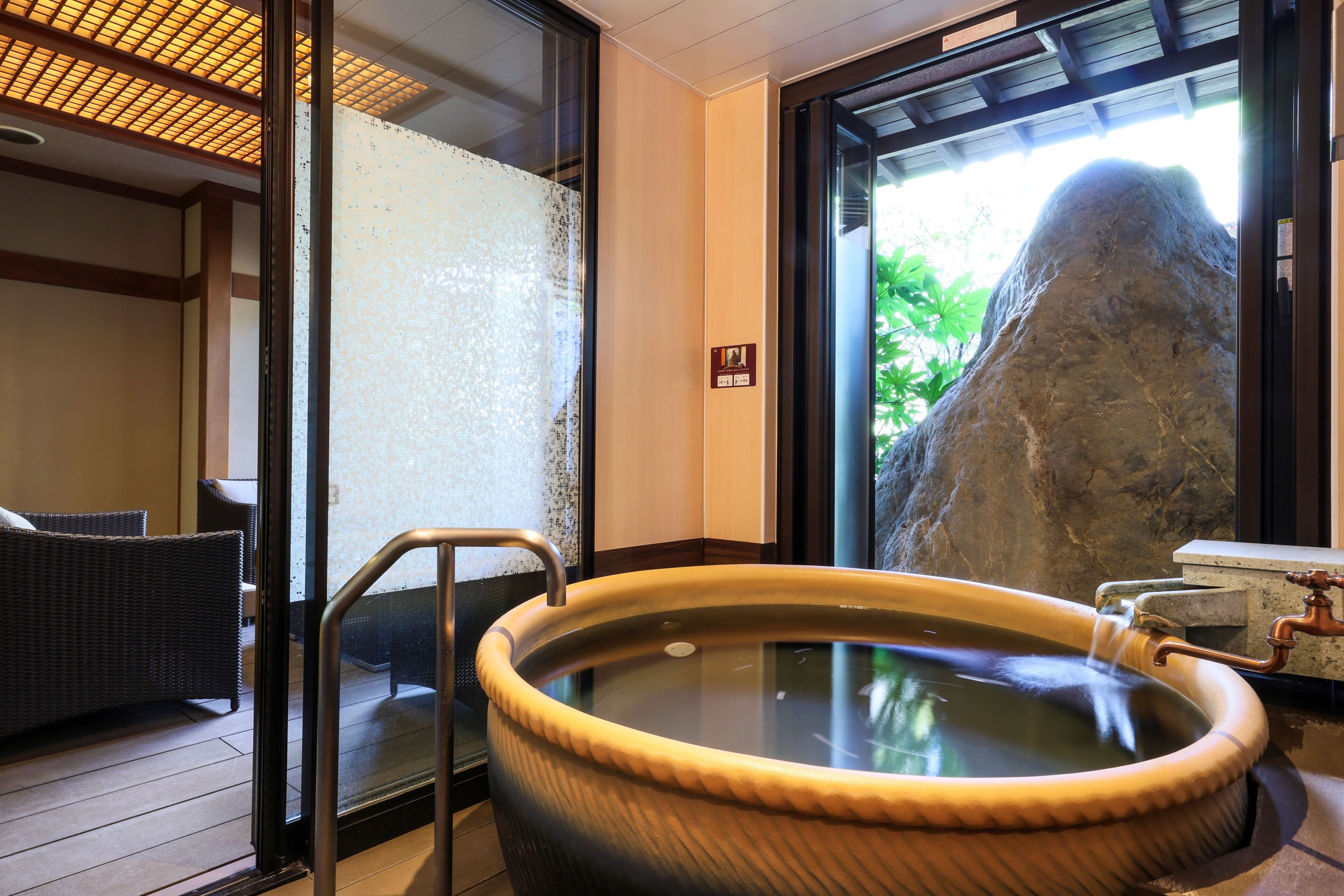 A hot tub with a stone wall and a view of greenery outside.