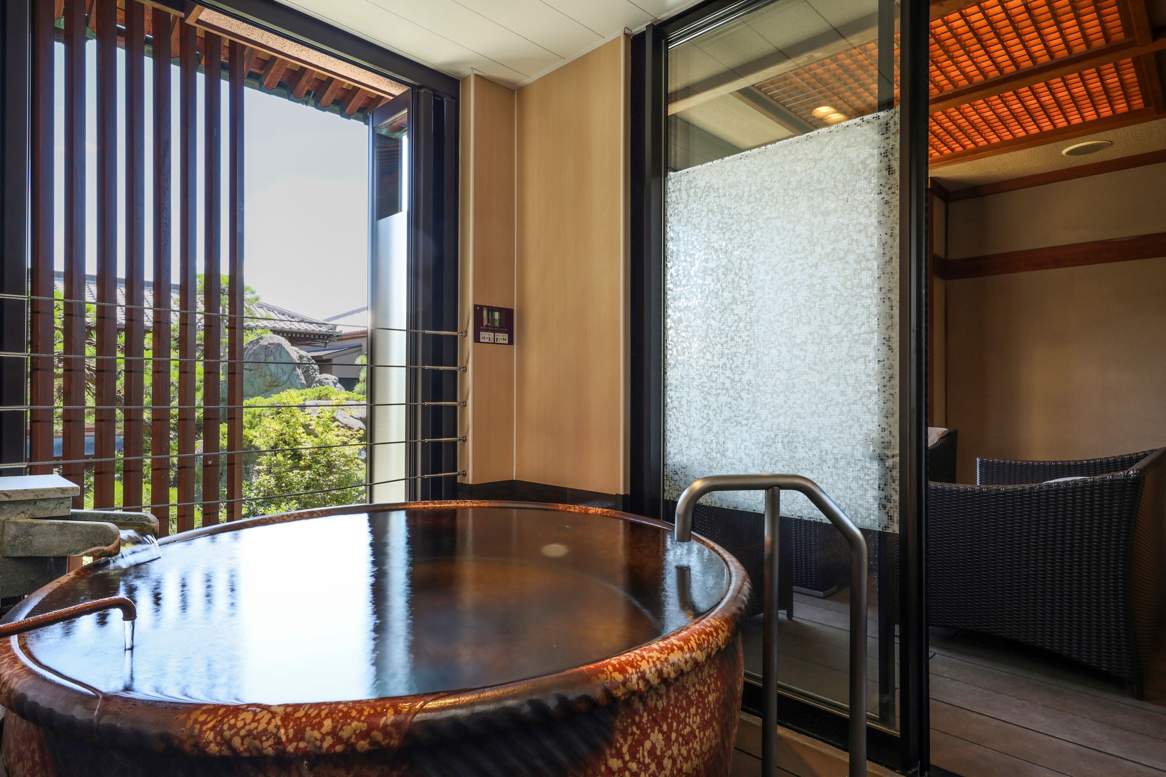 A hot tub with a metal ladder, a glass door leading outside, and a wicker chair inside.