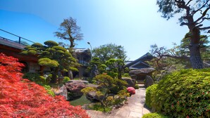 A traditional Japanese garden with a stone pathway leading to a building with a tiled roof. - Meiseki No Yado Kagetsu (Fuefuki)