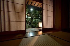 A traditional Japanese room with tatami flooring, shoji screens, and a view of a landscaped garden with rocks and a lamp. - Meiseki No Yado Kagetsu (Fuefuki)
