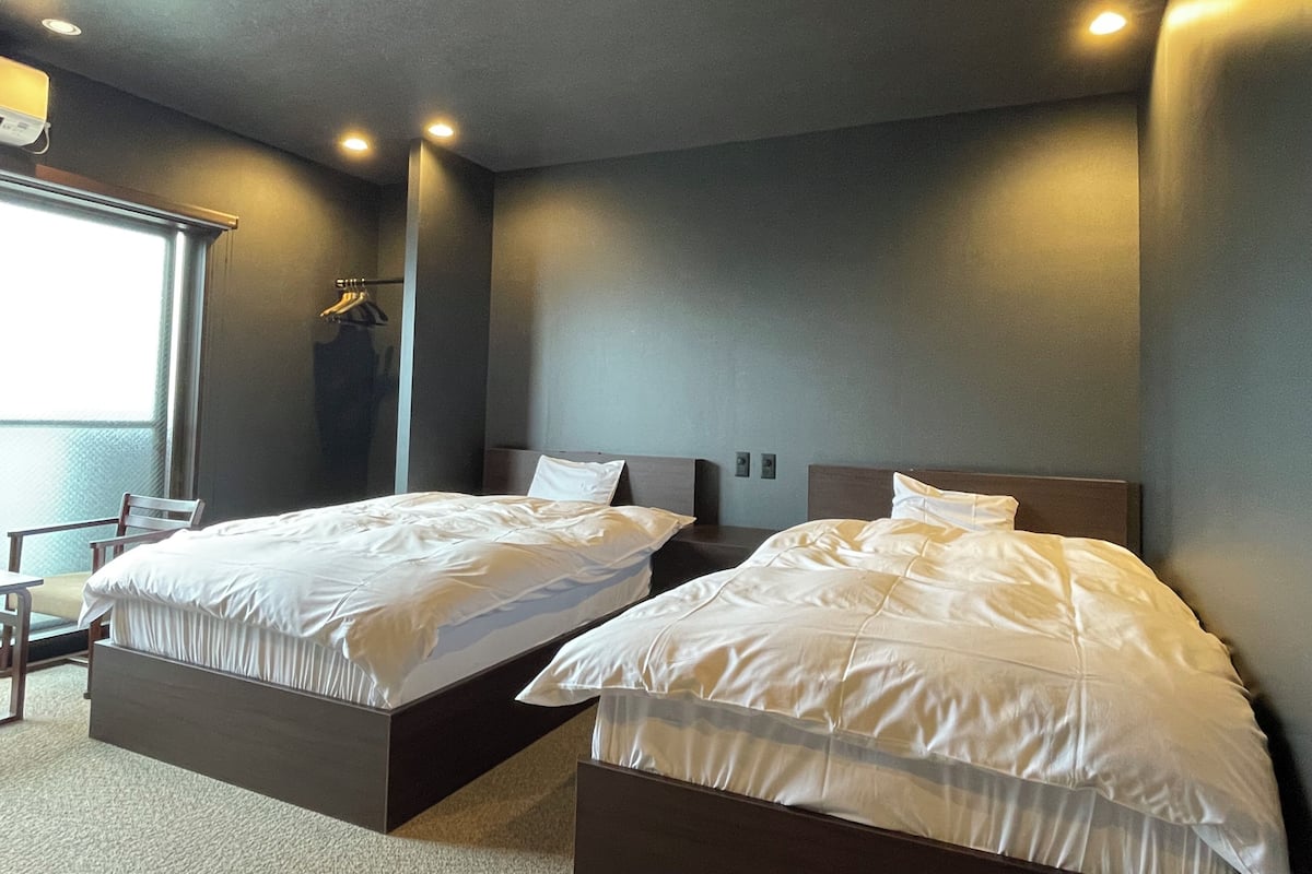 Une chambre d’hôtel avec deux lits, une chaise, une fenêtre et un porte-manteau.