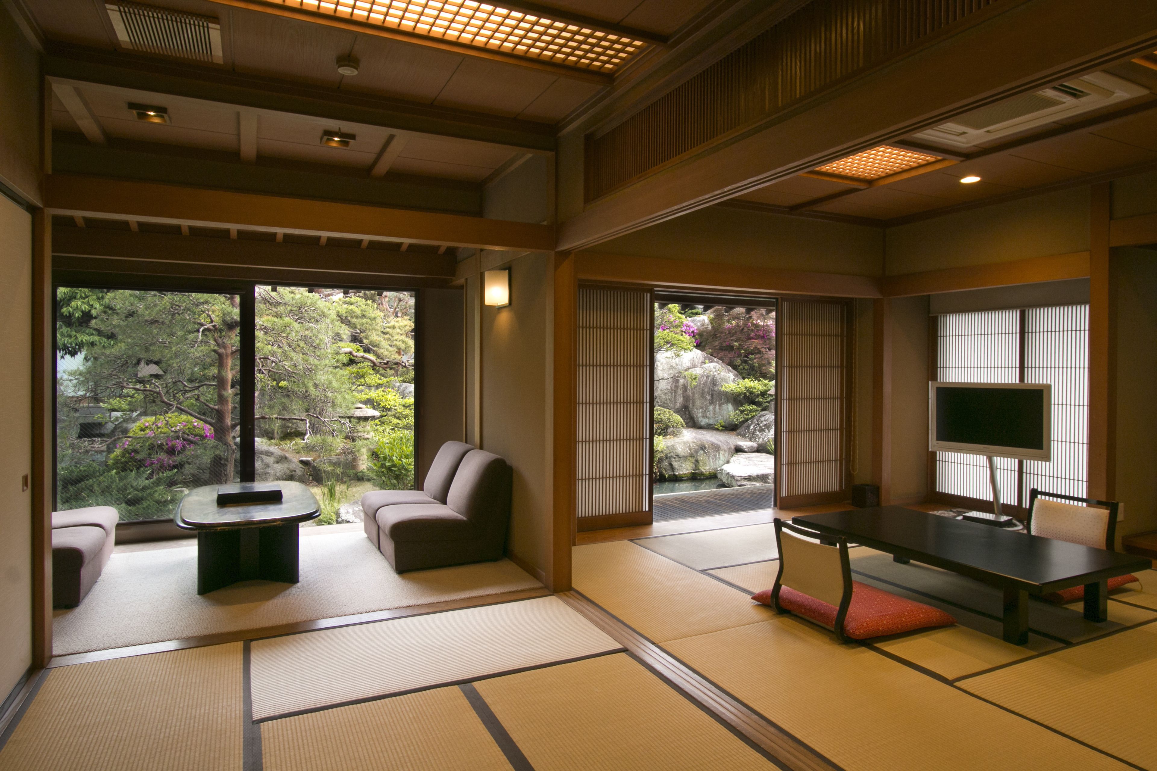Een traditionele Japanse kamer met tatami vloerbedekking, een lage tafel met kussens, een bank en een televisie.