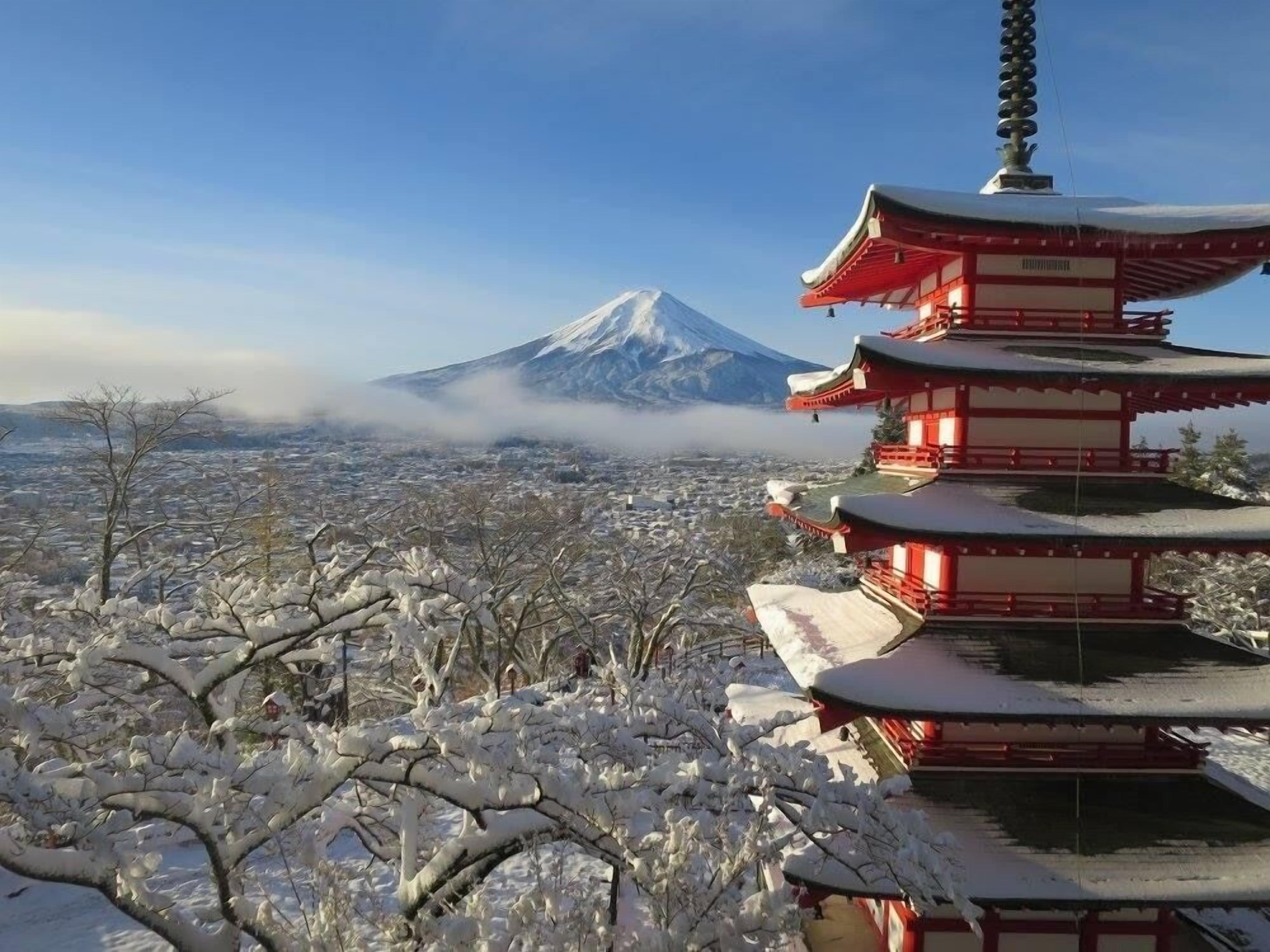 Eine traditionelle japanische Pagode mit mehreren Ebenen, umgeben von schneebedeckten Bäumen und Blick auf einen Berg im Hintergrund.