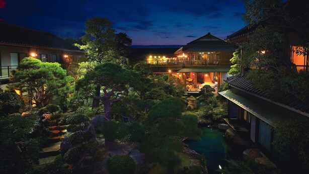 A traditional Japanese-style building with a koi pond, surrounded by lush greenery and illuminated by warm lighting. - Meiseki No Yado Kagetsu (Fuefuki)