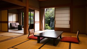 A traditional Japanese room with tatami flooring, a low table, and a view of a waterfall. - Meiseki No Yado Kagetsu (Fuefuki)