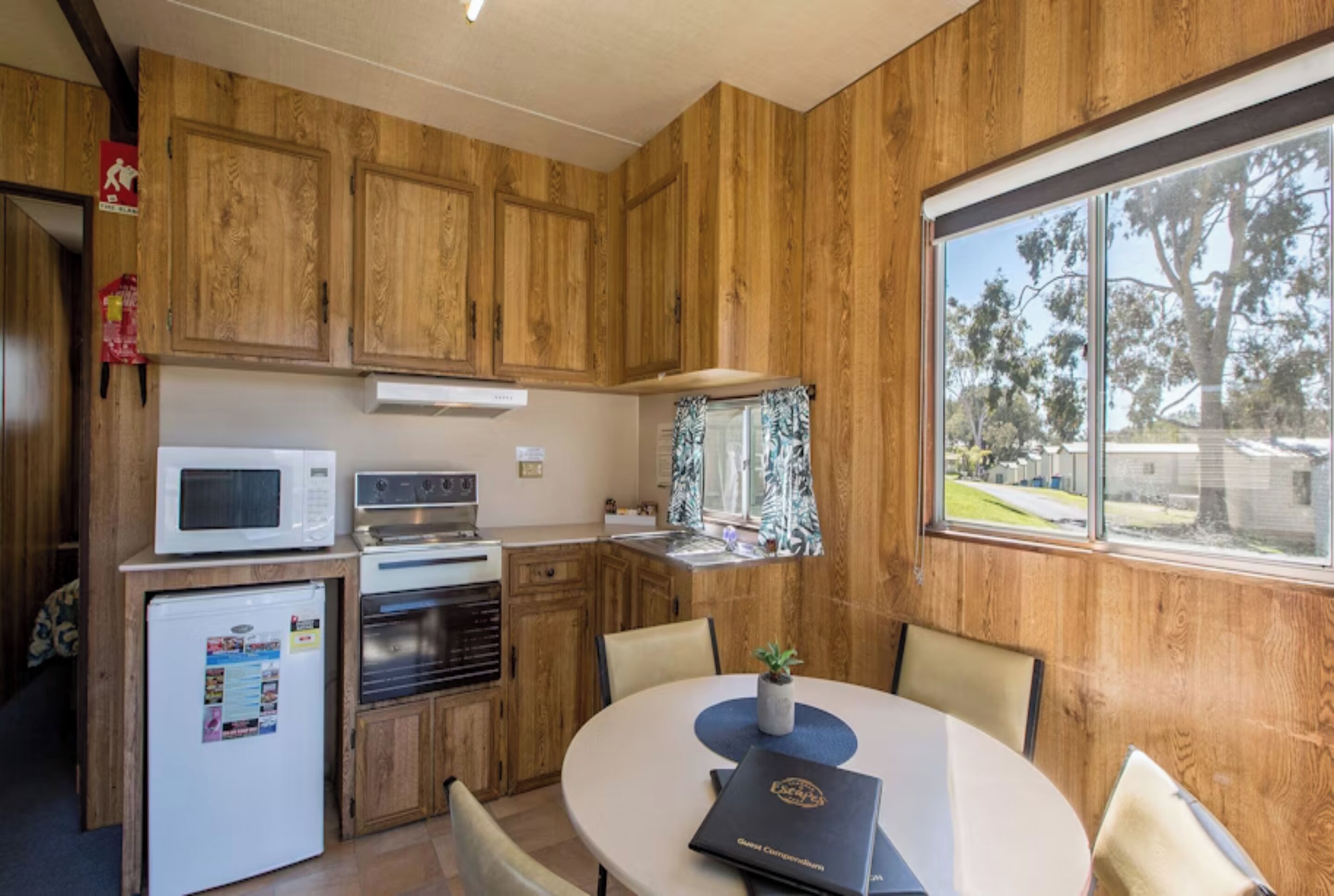 A compact kitchen with wooden cabinets, a microwave, a refrigerator, and a dining table with chairs.