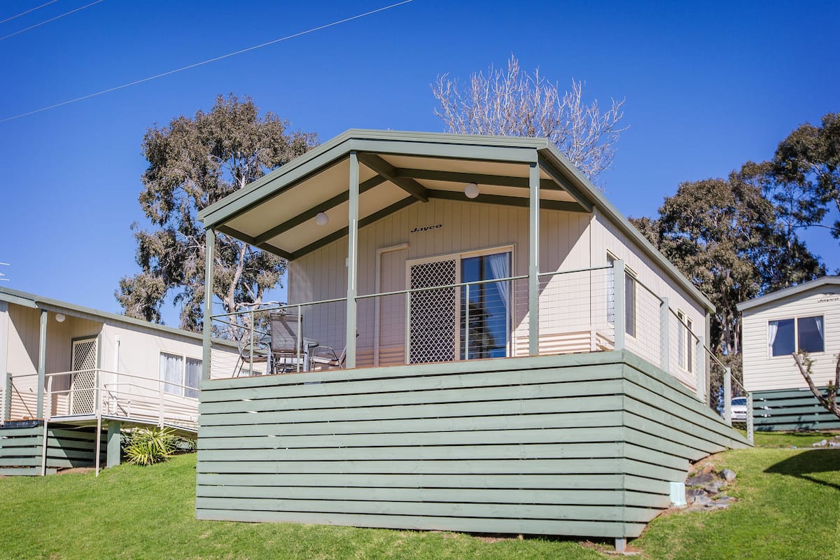 Ein eingeschossiges Mobilheim mit Veranda, überdachter Terrasse und einer Tür mit Fenster.