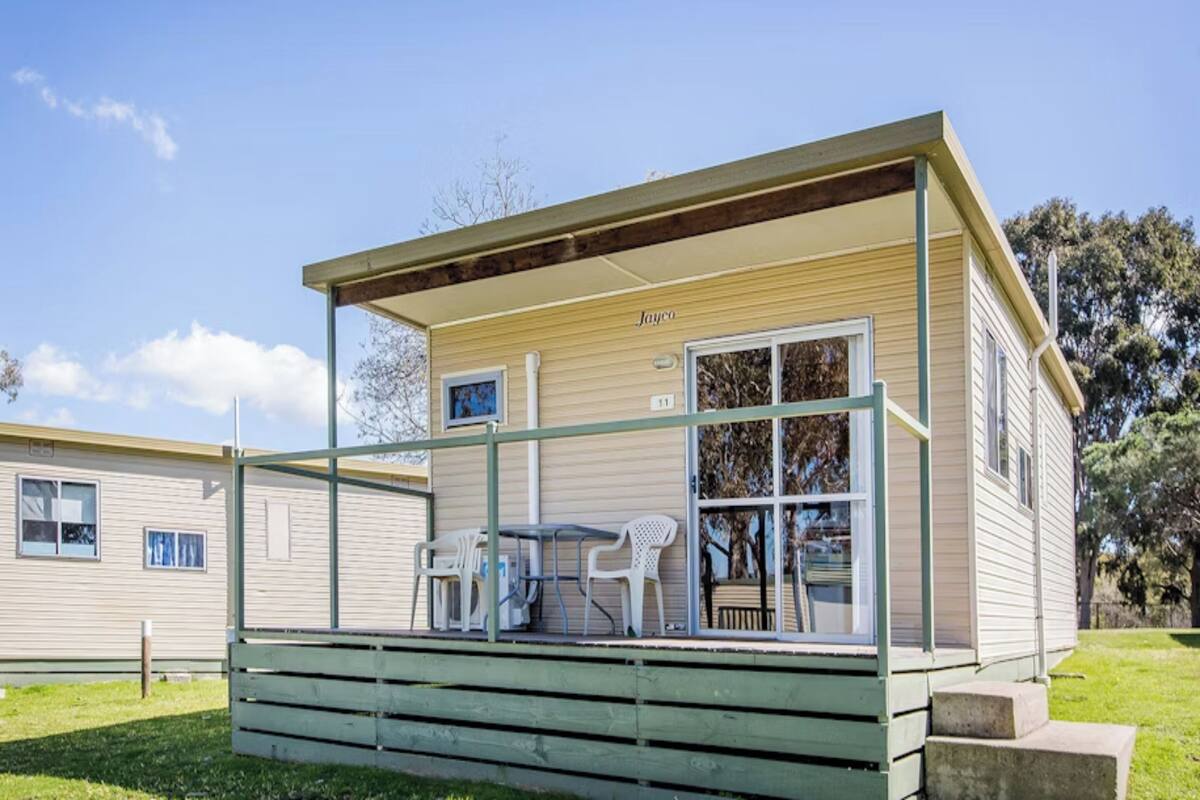 Ein kleines, eingeschossiges Mobilheim mit Veranda, Tisch und zwei Stühlen.